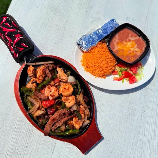 Sizzling fajitas with chicken, steak, shrimp, and vegetables, served with rice, beans, and tortillas.