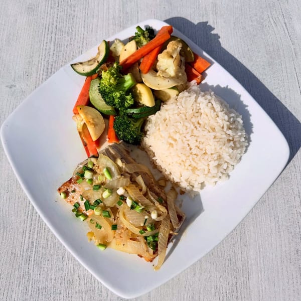 A white plate with a Mexican dish of fish topped with onions, rice, and mixed vegetables.