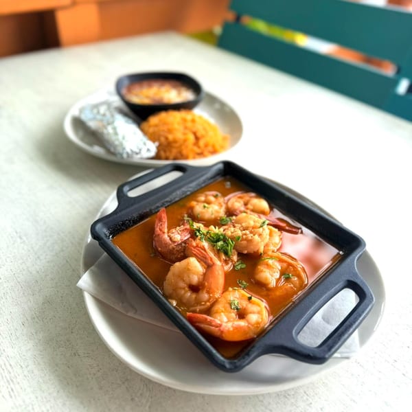 Shrimp in red sauce with cilantro in a black dish, with rice and beans in the background.