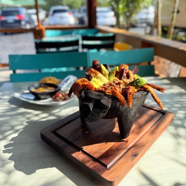 Mexican molcajete dish with meat, avocado, and lime, served on a wooden board outdoors.