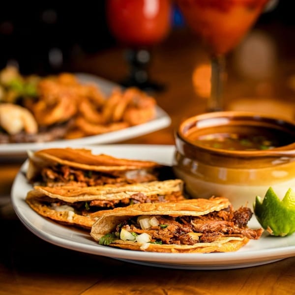 Three Chaparral Mexican birria tacos with a side of consommé and lime wedges.