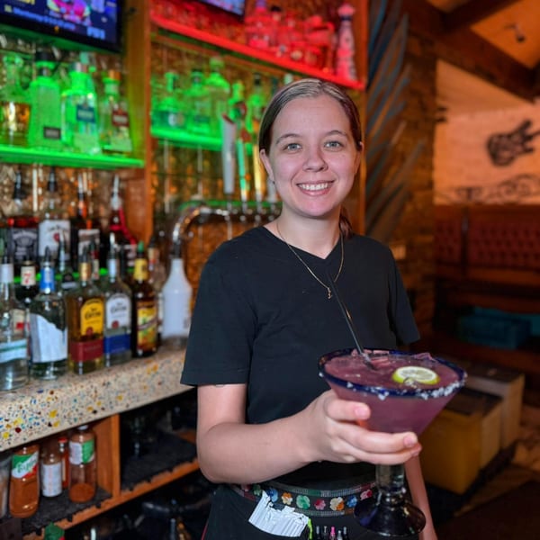 Smiling bartender holding a purple margarita with a lime slice at Chaparral Mexican Restaurant.
