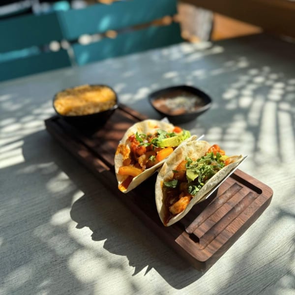 Two shrimp tacos with avocado and cilantro, served with sides of rice and beans.