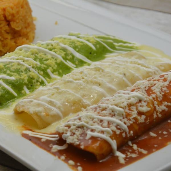 Three enchiladas with green, white, and red sauces, topped with cheese and sour cream, served with rice.