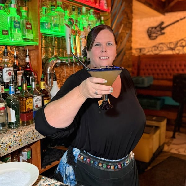 A smiling woman bartender holds a margarita at Chaparral Mexican and Cuban Restaurant.