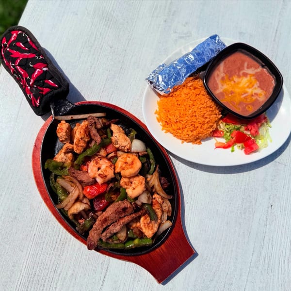 Sizzling fajitas with chicken, steak, shrimp, and vegetables, served with rice, beans, and tortillas.