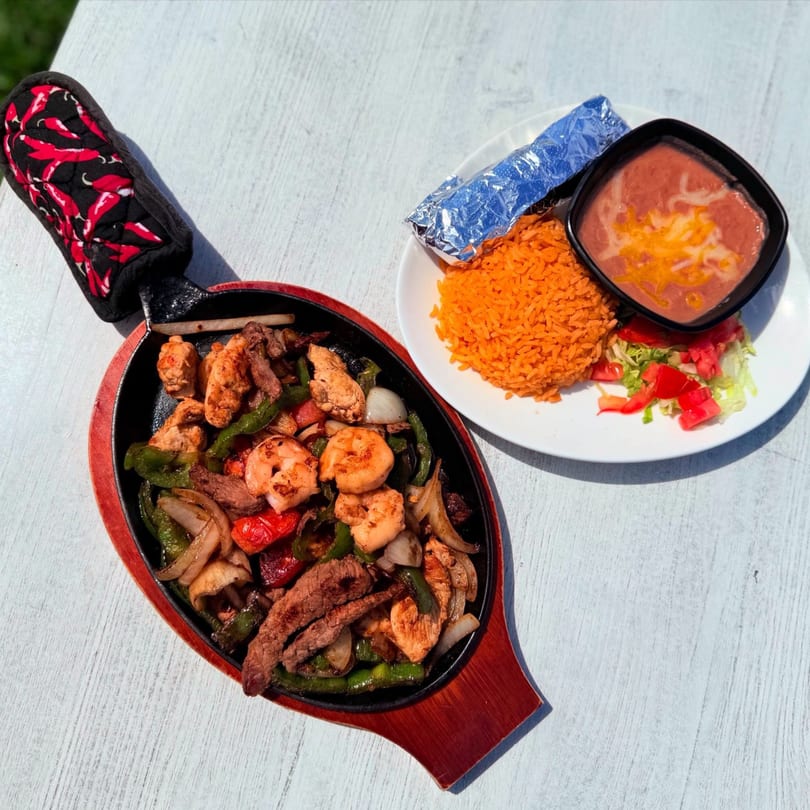 Sizzling fajitas with chicken, steak, shrimp, and vegetables, served with rice, beans, and tortillas.
