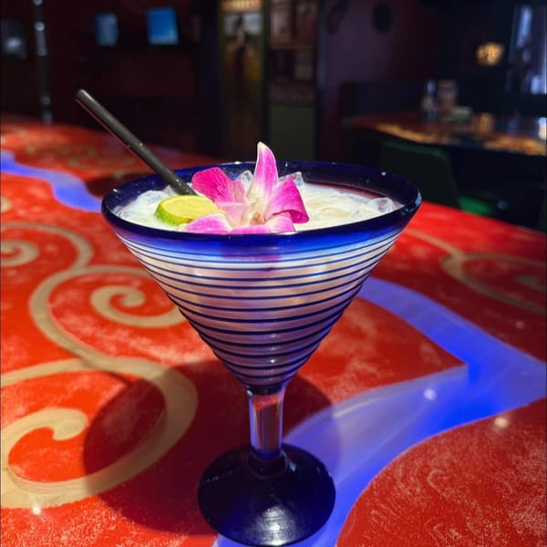 A Chaparral Mexican and Cuban Restaurant cocktail in a blue striped glass with a pink orchid and lime.