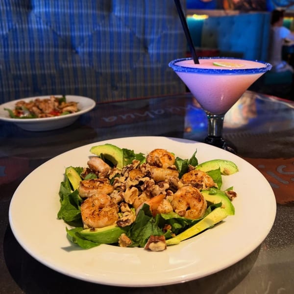 Shrimp and avocado salad with walnuts and a pink margarita with a lime garnish.