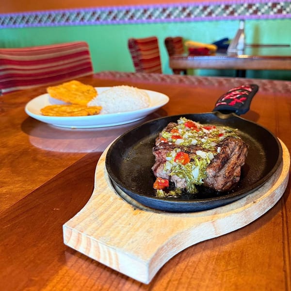 Sizzling steak with salsa, rice, and plantains on a wooden table at Chaparral Mexican and Cuban Restaurant.