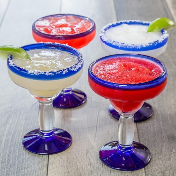 Four colorful margaritas, two red and two yellow, in blue-rimmed glasses with salt and lime.